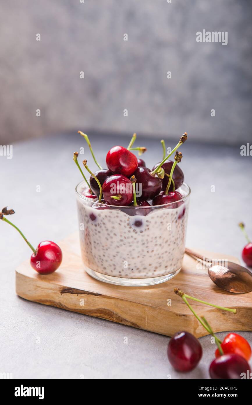 Budino di Chia con ciliegi, yogurt naturale, in un bicchiere su una superficie grigia. Messa a fuoco selettiva. Dessert sano, nutrizione adeguata, cibo super. Foto Stock