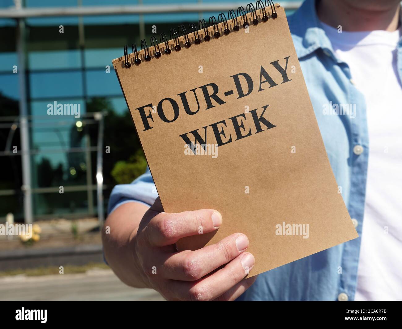 L'uomo propone il segno della settimana di quattro giorni. Blocco note in mano. Foto Stock