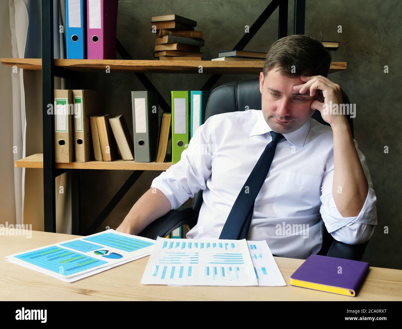 Un uomo d'affari stanco esamina la relazione finanziaria e i risultati dell'audit. Foto Stock