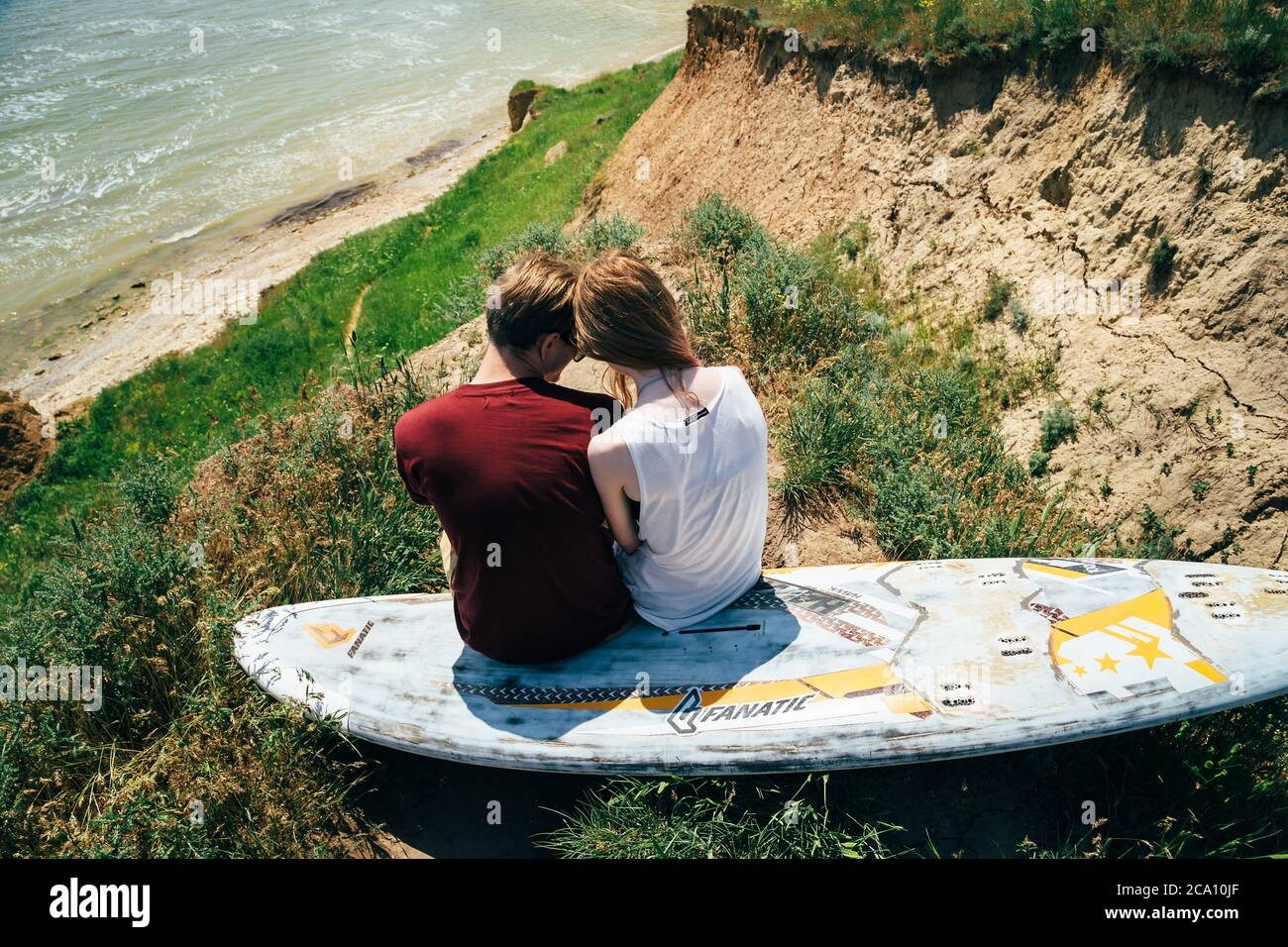 ODESSA, UCRAINA - MAGGIO, 20 2015: Carino giovane coppia hipster di surfisti con tavola da surf seduto sulla collina che guarda al mare. Vista posteriore Foto Stock