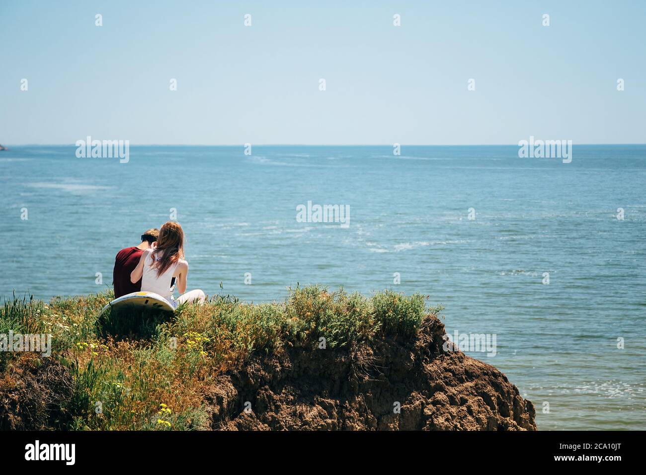 ODESSA, UCRAINA - MAGGIO, 20 2015: Carino giovane coppia hipster di surfisti con tavola da surf seduto sulla collina che guarda al mare. Vista posteriore Foto Stock
