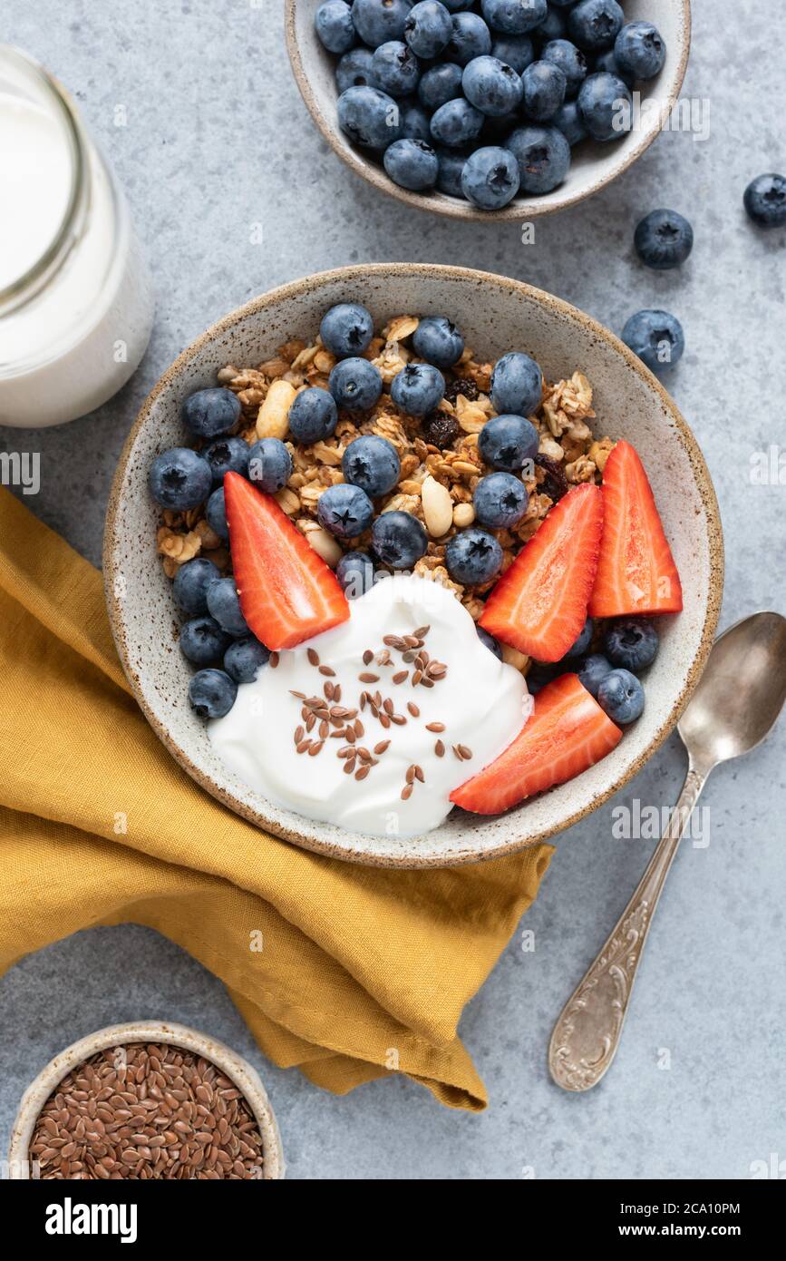 Recipiente di granola con frutti di bosco e yogurt su fondo di cemento. Sana colazione cibo vista dall'alto orientamento verticale Foto Stock
