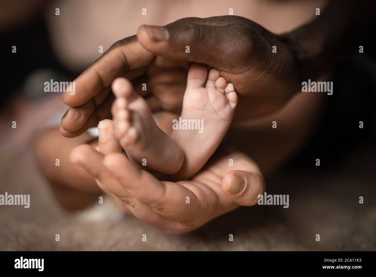 famiglia interrazziale che tiene i piedi del bambino in mani mescolate dal colore nero e bianco della pelle Foto Stock