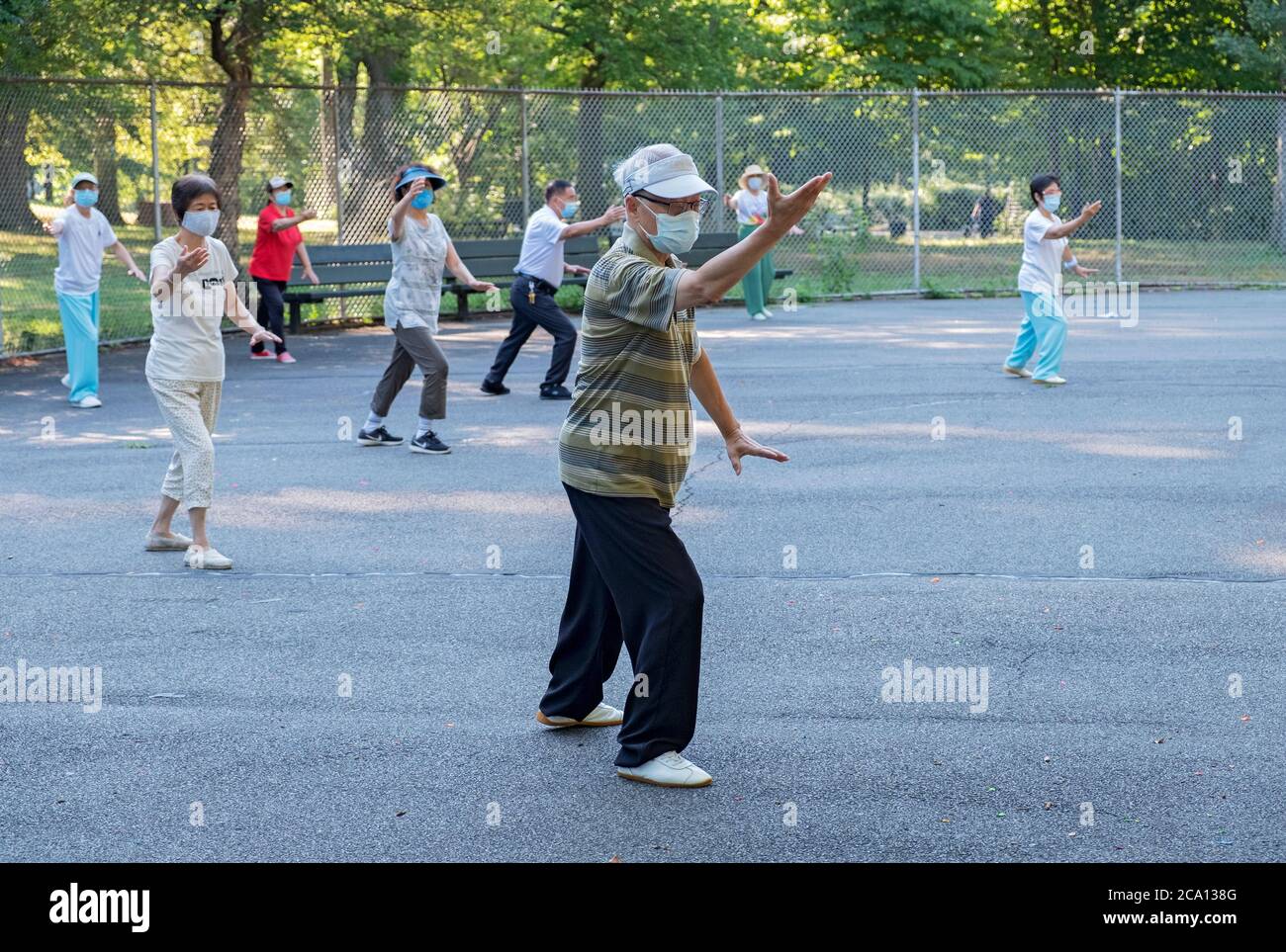 Uomini e donne di varie età ed etnie frequentano una lezione di Tai Chi al mattino indossando maschere chirurgiche e divaricatori sociali. In Queens, New York City. Foto Stock