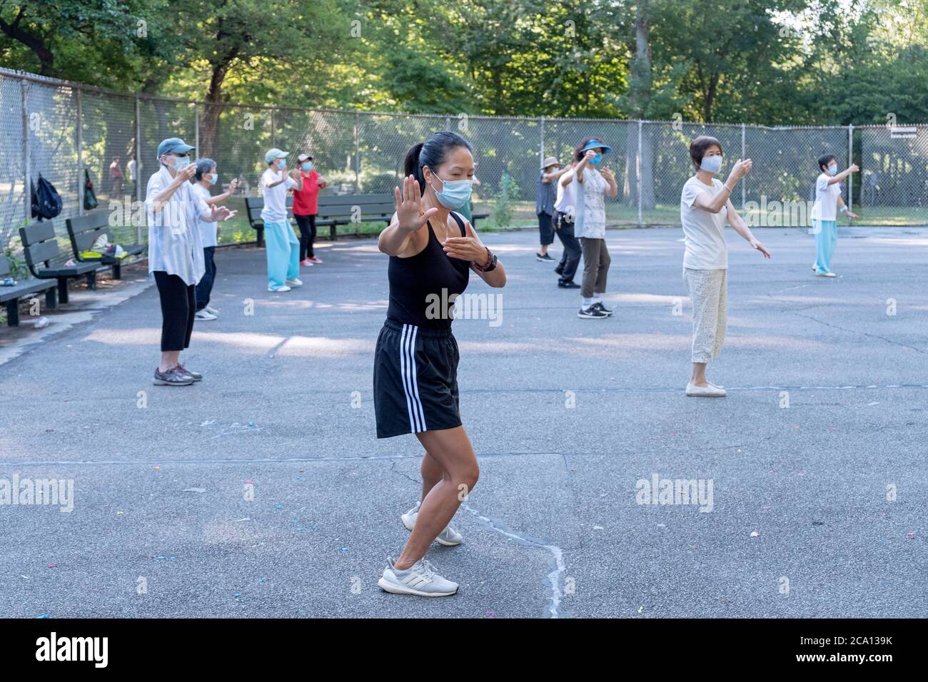 Donne di varie età ed etnie frequentano una lezione di Tai Chi al mattino che indossa maschere chirurgiche e divaricazioni sociali. In Queens, New York City. Foto Stock