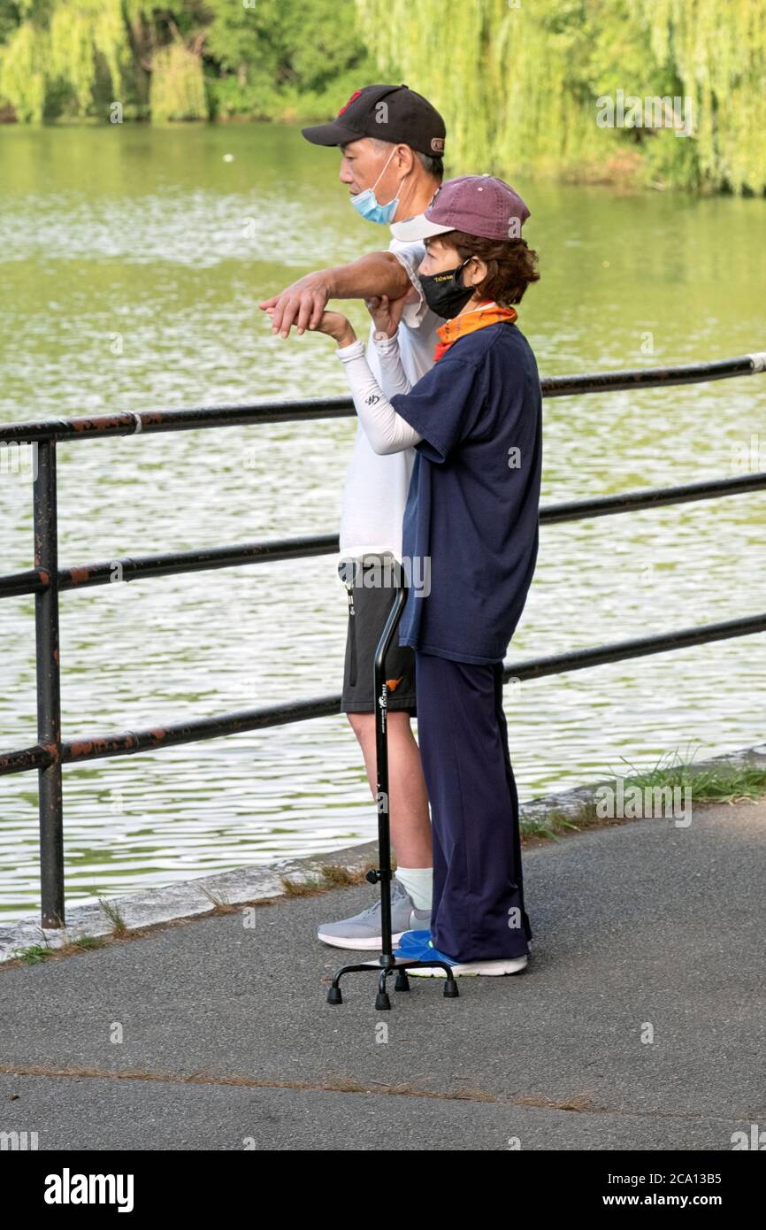 Un aiuto aiuta un uomo con problemi di salute a fare la sua routine di stretching. In un parco a Flushing, Queens, New York City. Foto Stock