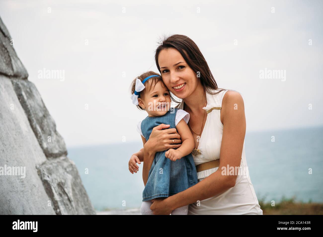 Felice giovane madre con una piccola figlia in mani che abbracciano vicino al faro, sfondo all'aperto Foto Stock