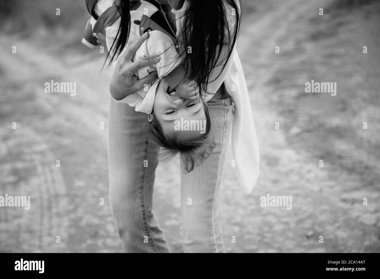 Felice giovane madre che gioca con una piccola figlia, tenendo la bambina capovolta, sfondo esterno Foto Stock