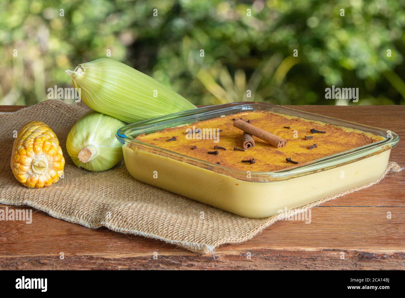 Canjica. Curau. Dolci tipici brasiliani per la festa della junina. Pannocchie di mais. Sfondo verde sfocato. Dessert brasiliano Foto Stock