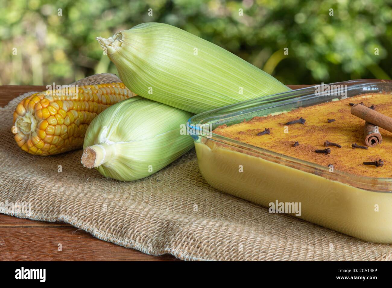 Canjica. Curau. Dolci tipici brasiliani per la festa della junina. Pannocchie di mais. Sfondo verde sfocato. Dessert brasiliano Foto Stock
