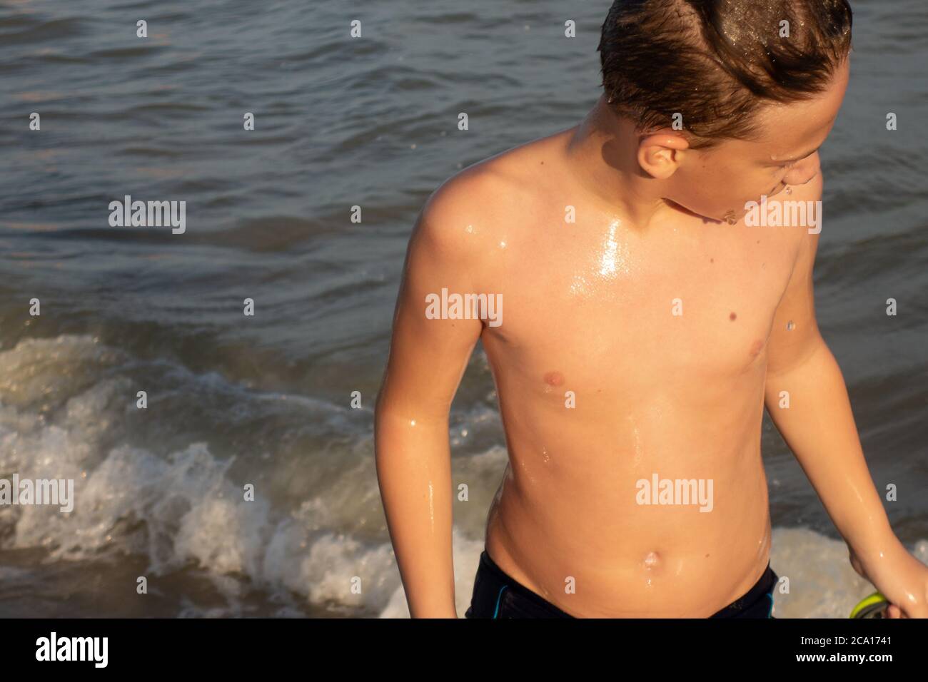 Un bel ragazzo di 10 anni esce dall'acqua in riva al mare al tramonto. Foto Stock