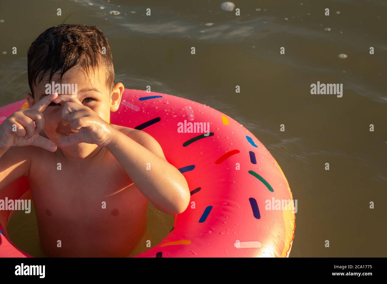 Un ragazzo di 5 anni nuota in mare con un cerchio gonfiabile a forma di ciambella e racconta che grande medusa ha appena visto in mare. Foto Stock