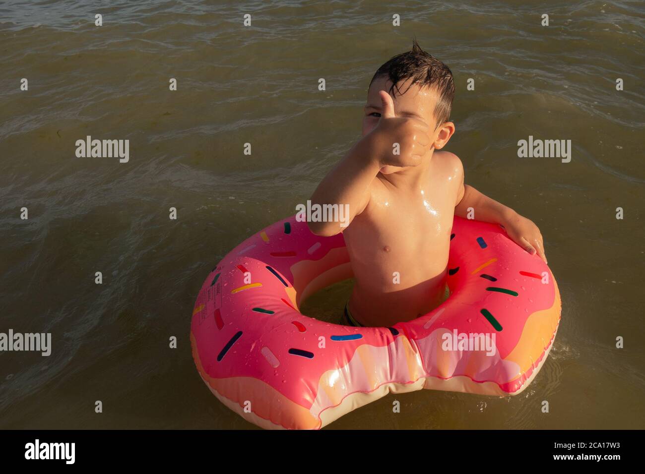 Un ragazzo di 5 anni nuota in mare con un cerchio gonfiabile a forma di ciambella e mostra un simile. Foto Stock