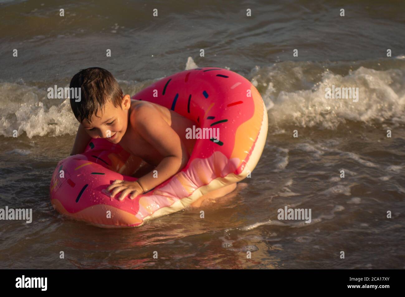 Un ragazzo allegro di 5 anni nuota in mare su un anello gonfiabile sotto forma di una ciambella in una giornata di sole. Foto Stock