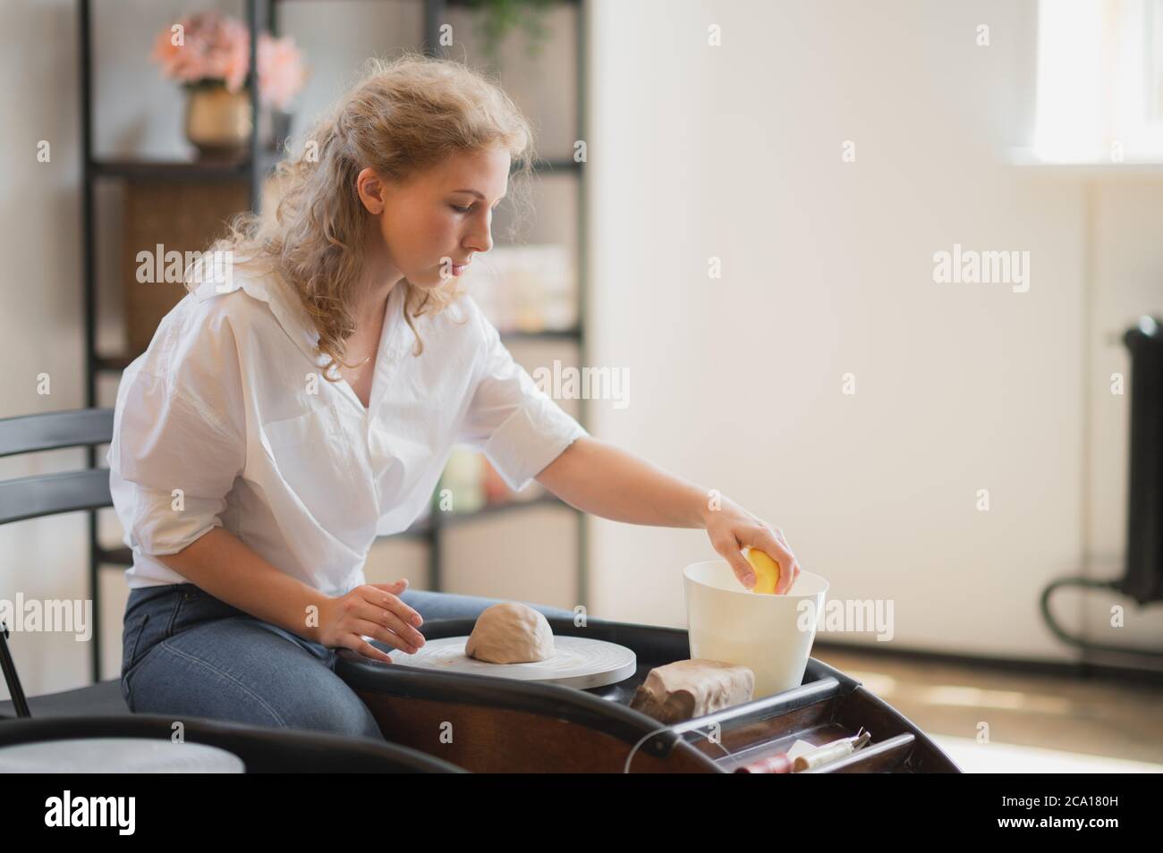 Vista ravvicinata delle mani della donna che lavorano sulla ruota in ceramica e che fanno pentola di argilla. Le mani scolpisce una tazza da pentola di argilla. Workshop sulla modellazione del vasaio Foto Stock