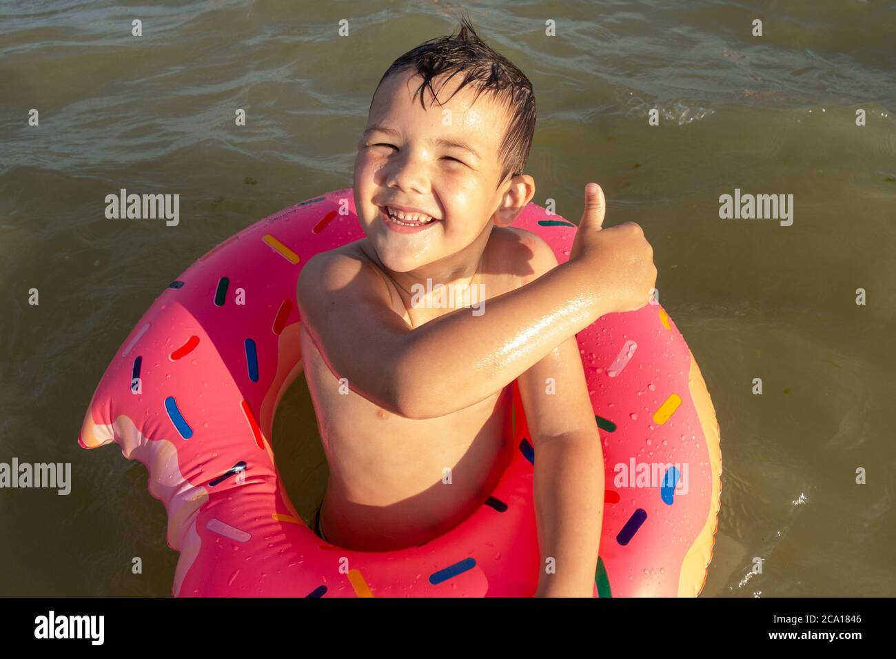 Un ragazzo di 5 anni nuota in mare con un cerchio gonfiabile a forma di ciambella e mostra un simile. Foto Stock