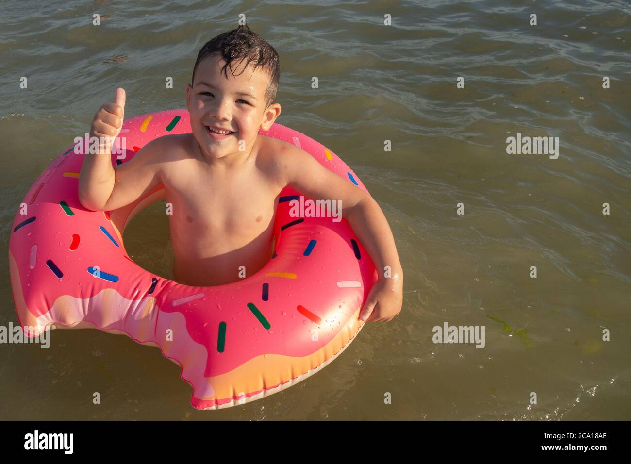 Un ragazzo di 5 anni nuota in mare con un cerchio gonfiabile a forma di ciambella e mostra un simile. Foto Stock