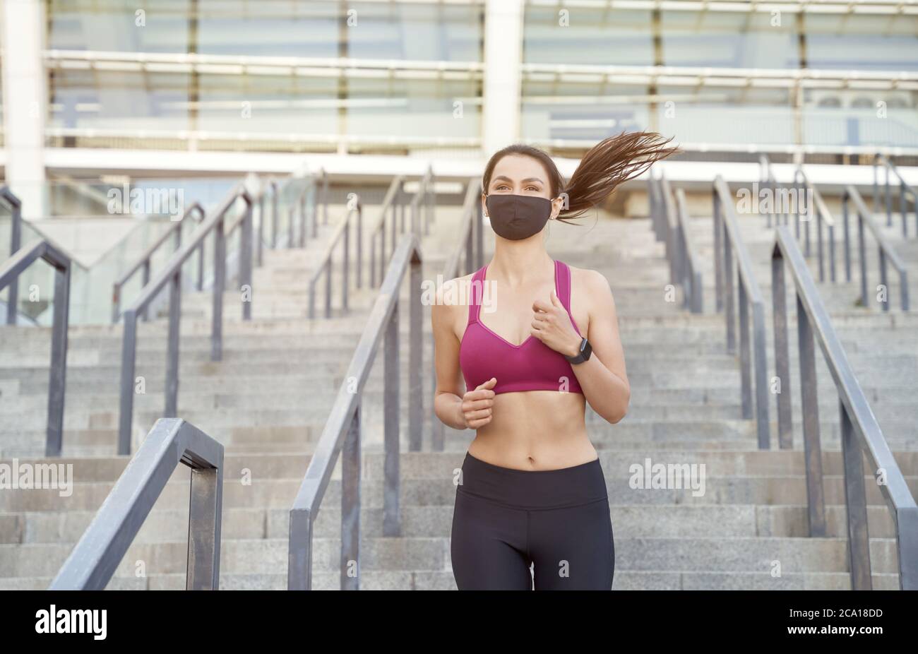 Correre in sicurezza durante l'epidemia. Giovane atletica in abiti sportivi con maschera protettiva che corre al piano inferiore in città durante la pandemia del coronavirus. Covid 19 e attività fisica, sport Foto Stock