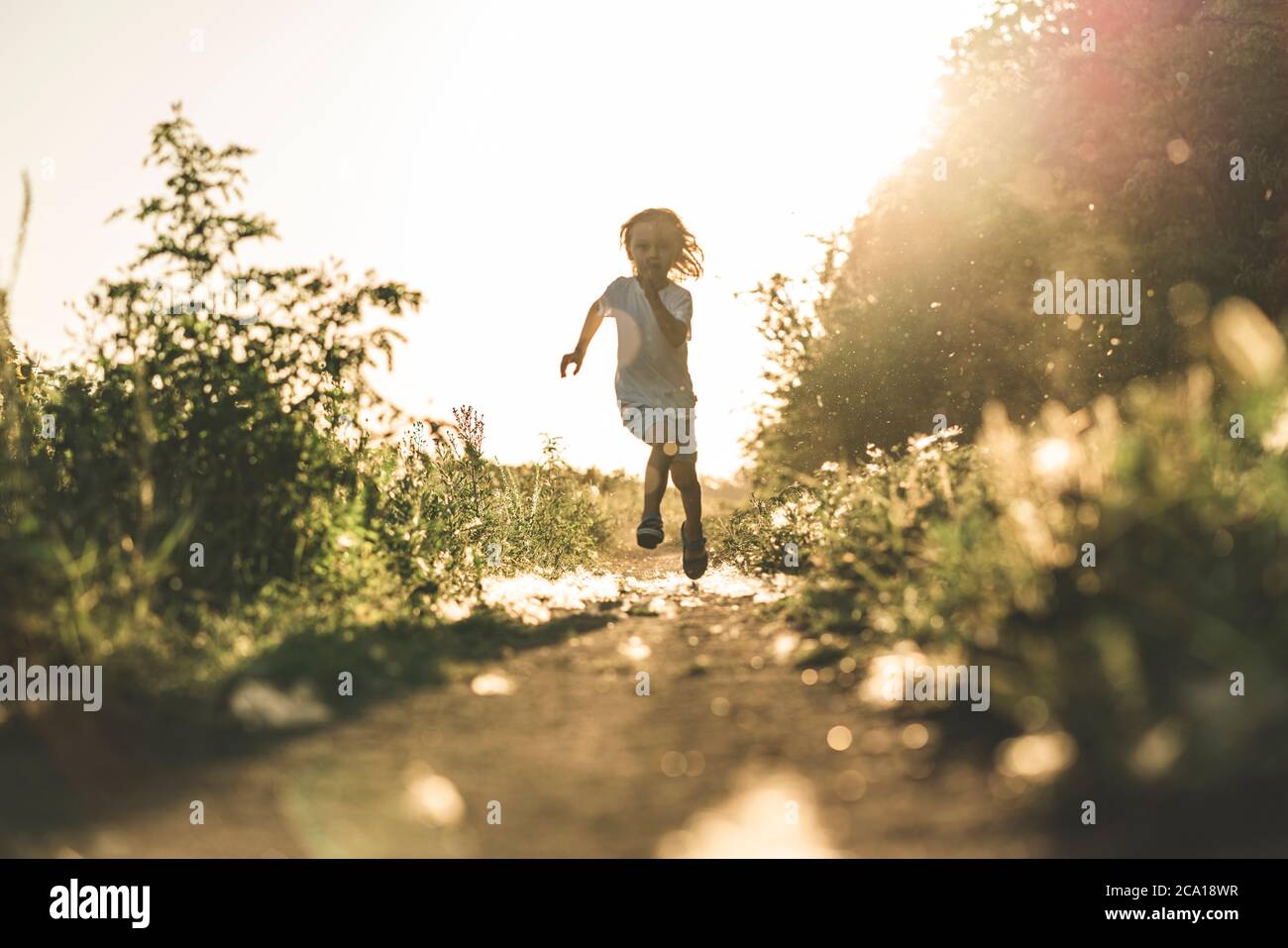 Un ragazzino corre lungo la strada al tramonto godendo della vita e della natura. Felice capretto in campagna. Silhouette di un ragazzo nei raggi solari. Aria fresca, concetto di ambiente. Foto Stock