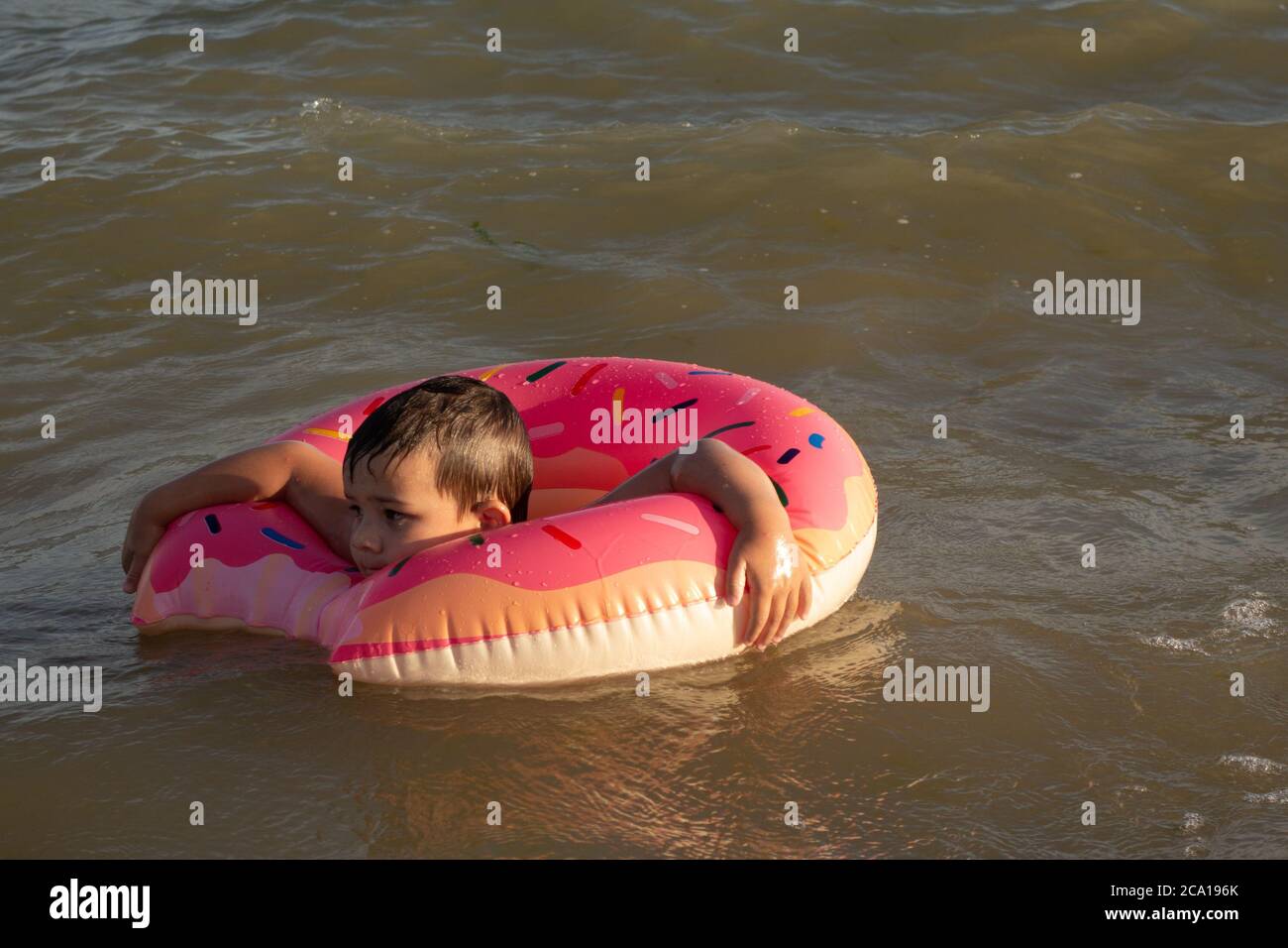 Un ragazzo allegro di 5 anni nuota in mare su un anello gonfiabile sotto forma di una ciambella in una giornata di sole. Foto Stock