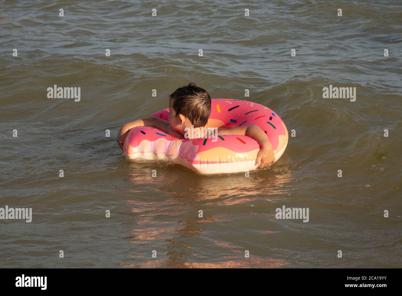 Un ragazzo allegro di 5 anni nuota in mare su un anello gonfiabile sotto forma di una ciambella in una giornata di sole. Foto Stock
