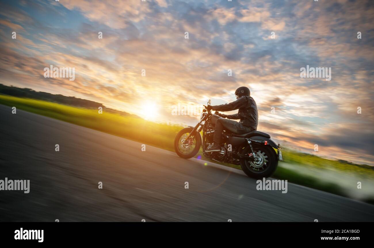 Motociclista scuro che guida moto ad alta potenza in natura con splendida luce del tramonto. Viaggi e trasporto. Libertà di guidare in moto Foto Stock