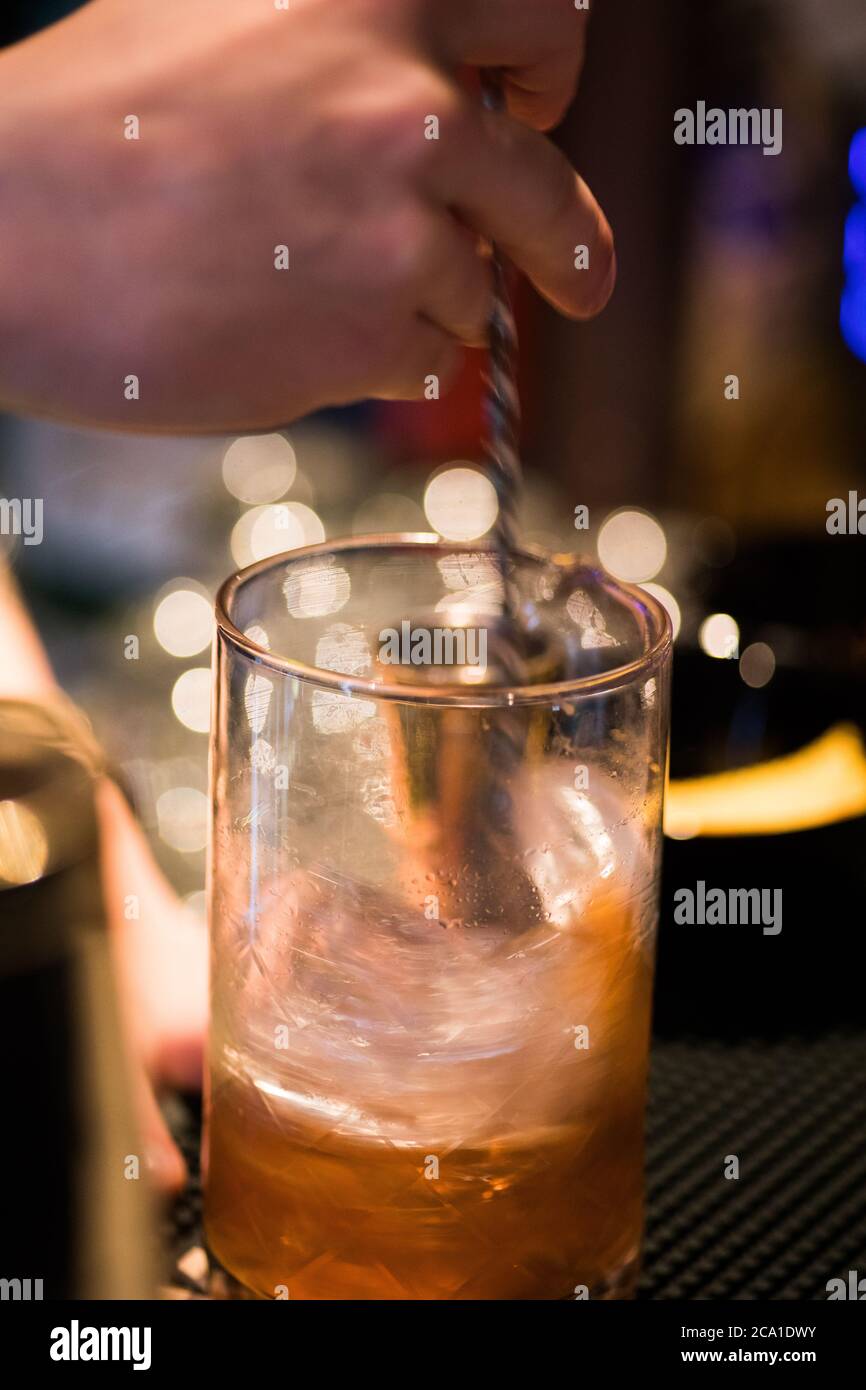 Primo piano della mano di un barman preparazione di un cocktail e agitazione in un bicchiere con ghiaccio, con sfocatura del movimento. Foto Stock