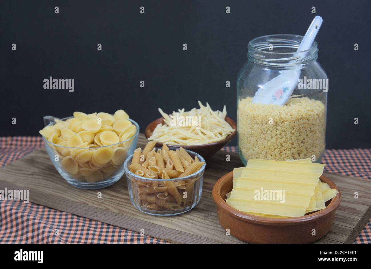 Un tavolo con vari contenitori con alcune paste italiane come i maccheroni integrali, le orecchiette, i trofie, le piastre per i cannelloni e le lettere per s. Foto Stock