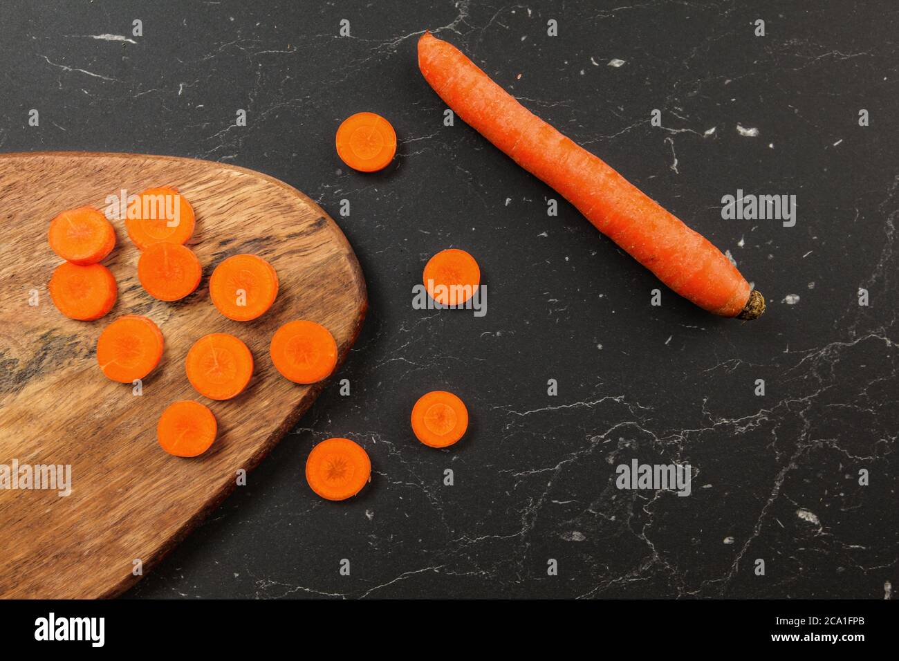 Carote affettate a piccoli cerchi e tagliere, una intera accanto ad essa su scrivania nera, foto dall'alto Foto Stock