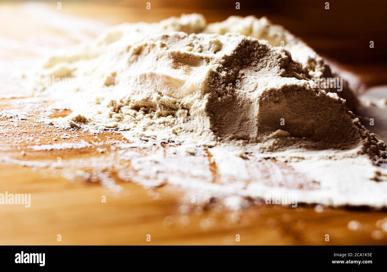 un mucchio di farina su un asse di legno pronto per essere impastato e cotto. Preparazione di alimenti a base di farina prima di essere cotti Foto Stock