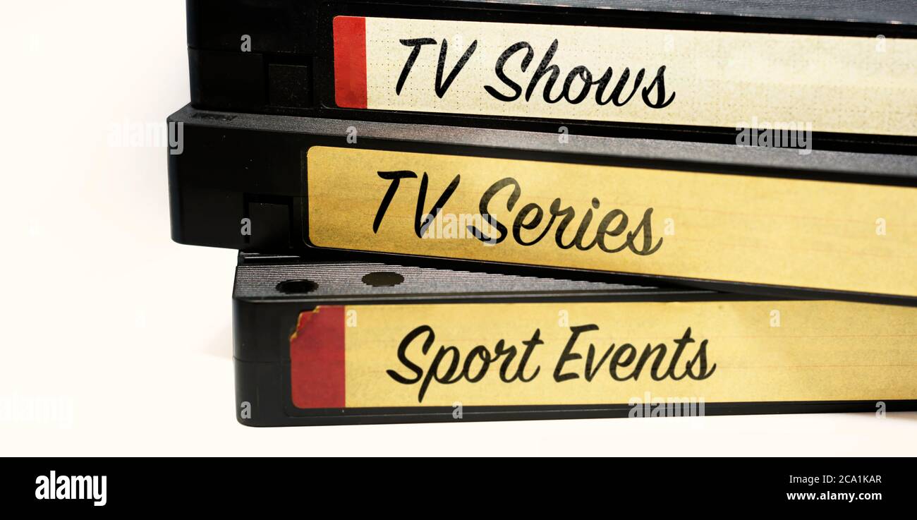 Nastri VHS impilati e con etichette che indicano i vari generi di intrattenimento televisivo registrati sul nastro su sfondo bianco. Foto Stock