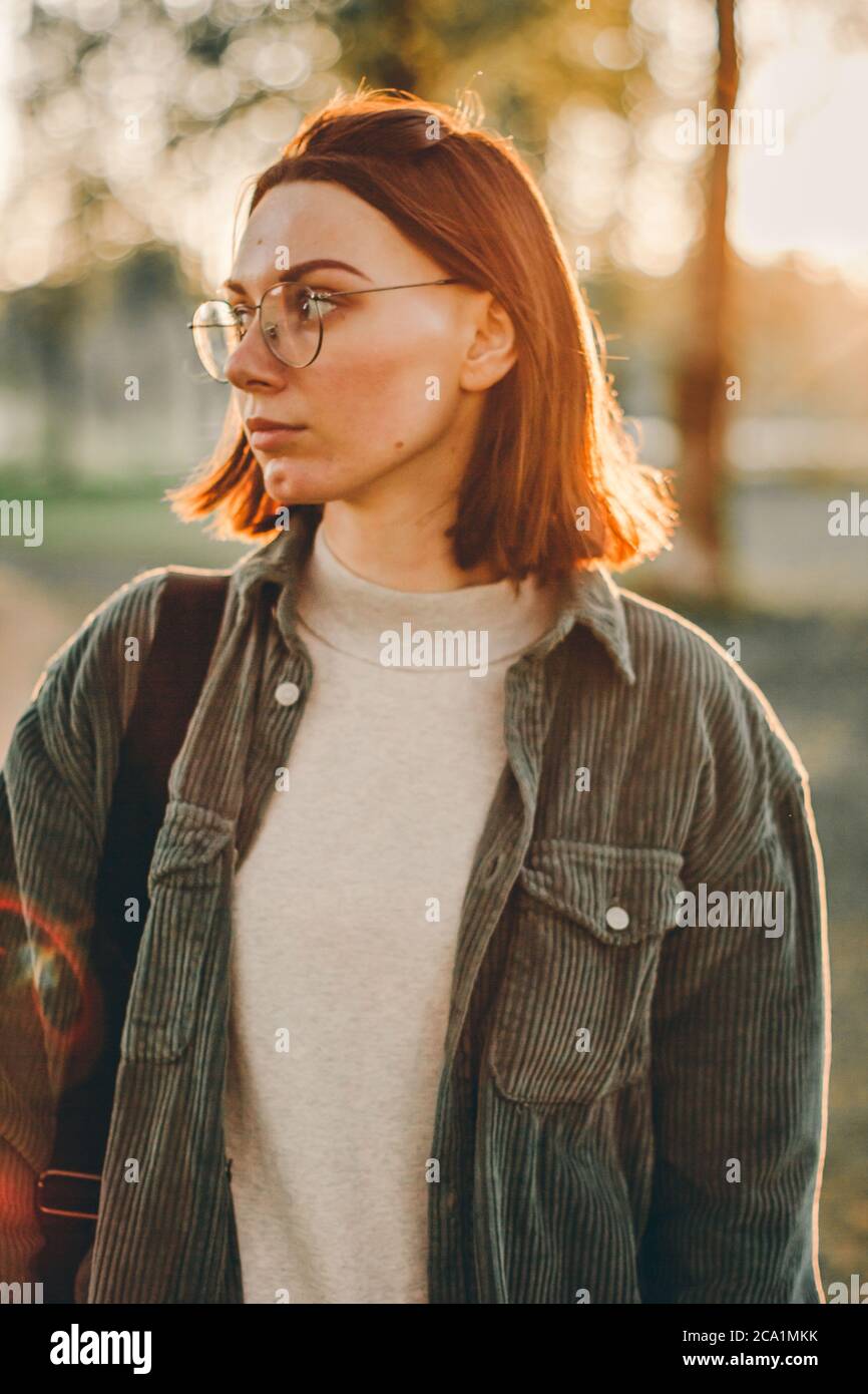 Closeup ritratto esterno di bella giovane donna caucasica con capelli corti brunette che indossano magliette e occhiali di jeans. Estate soleggiata sera par Foto Stock