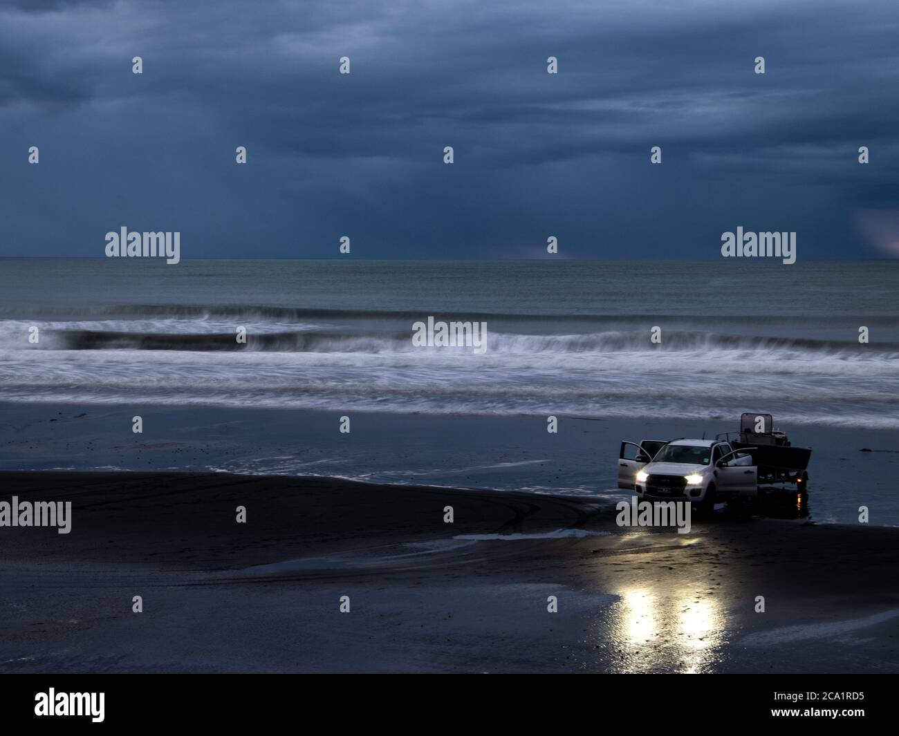 auto con luci accese sulla spiaggia bagnata sabbia a fine giornata con onde e nuvoloso cielo Foto Stock