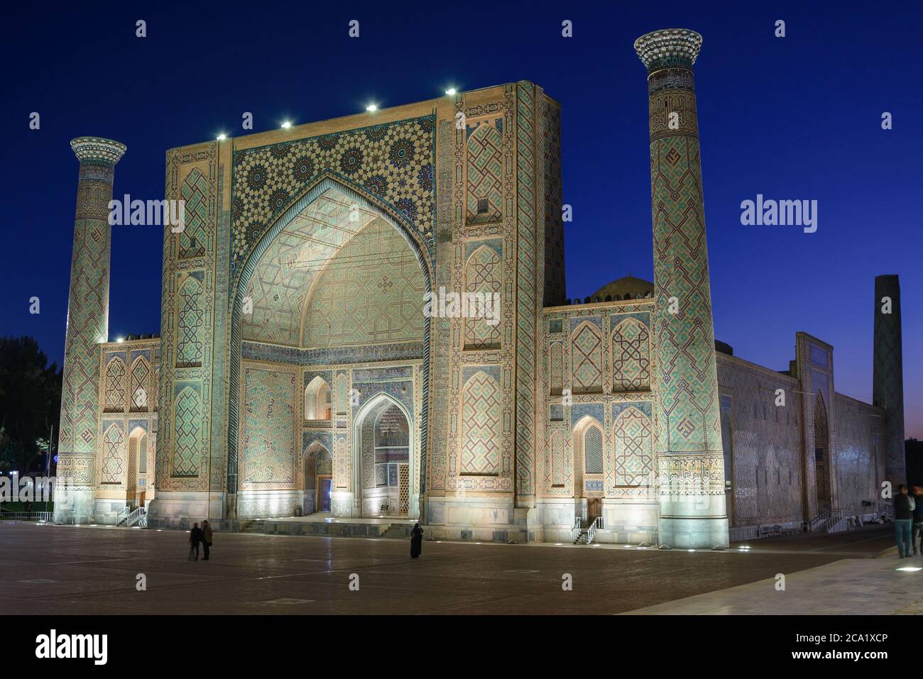 Ulugh Beg Madrasah illuminato di notte in Registan, Samarcanda, Uzbekistan. Edificio islamico con torri e grande iwan decorato con piastrelle in ceramica Foto Stock