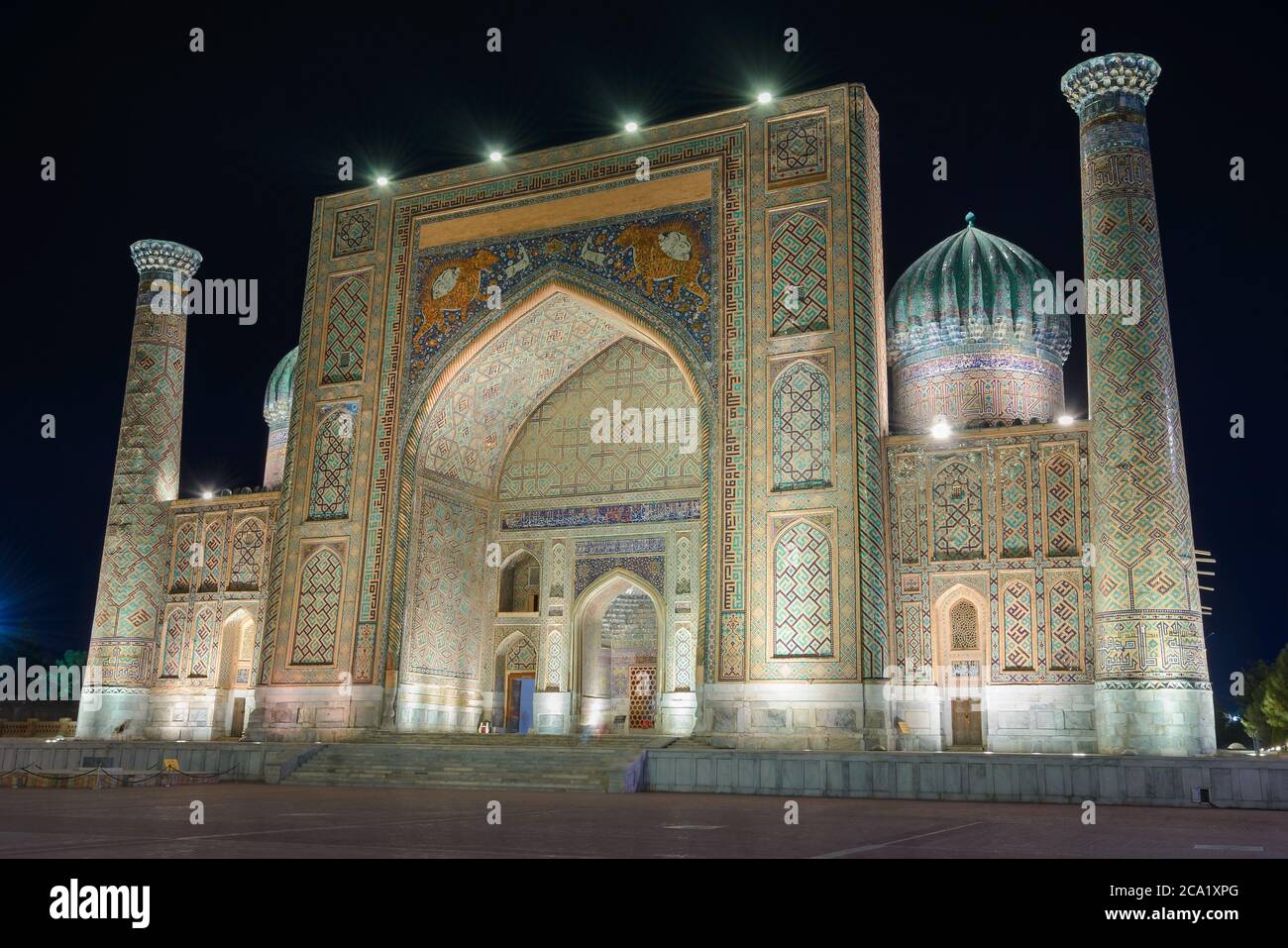 Sher Dor Madrasah di notte a Samarcanda, Uzbekistan. Edificio islamico con iwan e cupole scanalate decorate con mosaico. Shir Dar madrassa illuminato. Foto Stock
