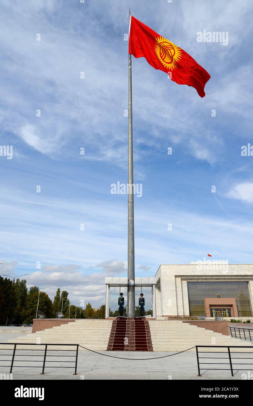 Palo della bandiera del Kirghizistan sorvegliato da due guardie d'onore in Piazza Ala Too a Bishkek con il Museo storico del Kirghizistan alle spalle. Foto Stock