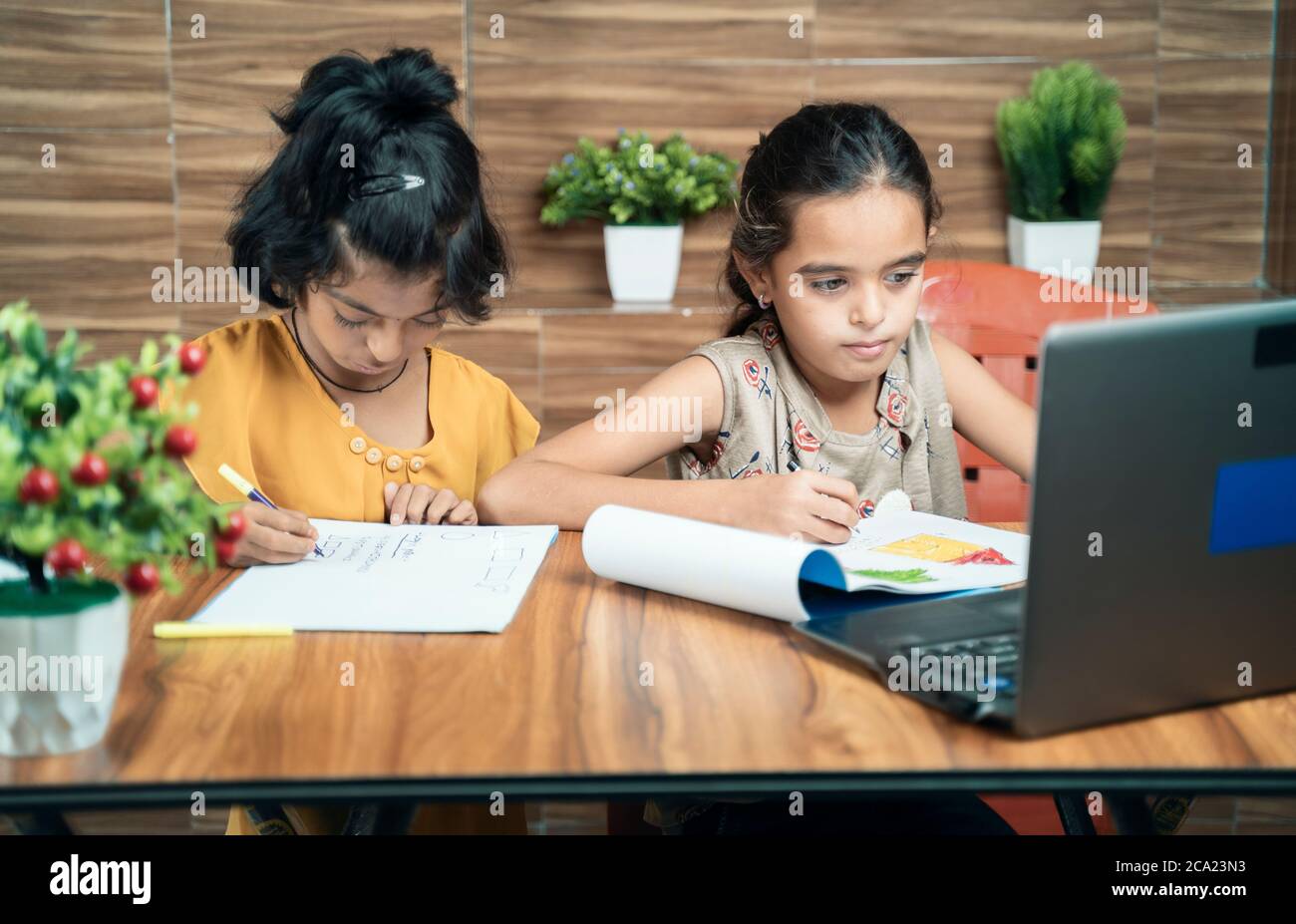 Due bambini impegnati nella scrittura guardando nel portatile durante la lezione online o virtuale a casa - concetto di e-learning o di apprendimento a distanza o bambini Foto Stock