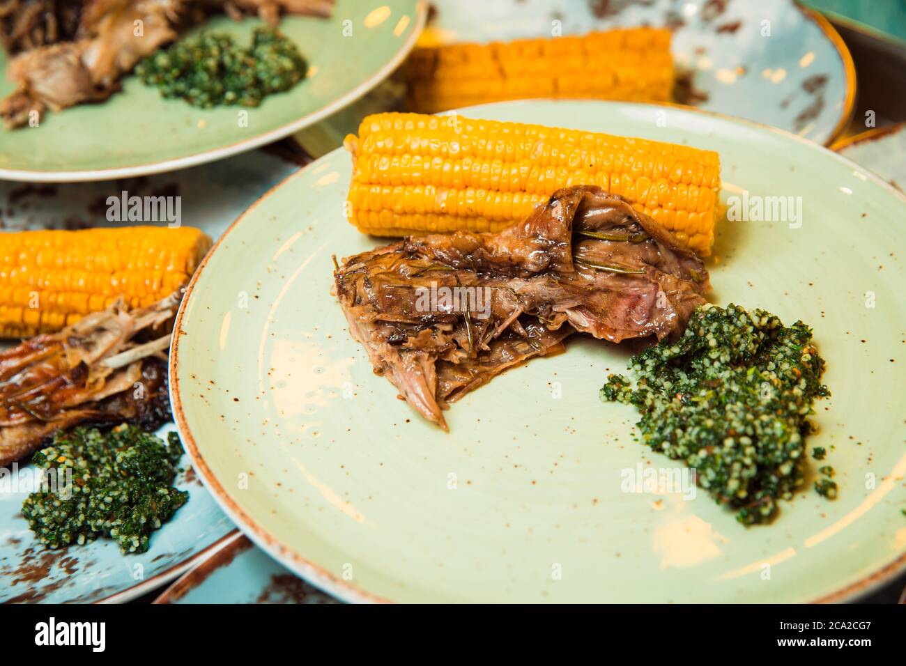 Sulla costata di mais e salsa verde viene servita della carne succosa preparata di fresco. Il cibo si trova su una piastra rotonda. Pronto a servire. Foto Stock