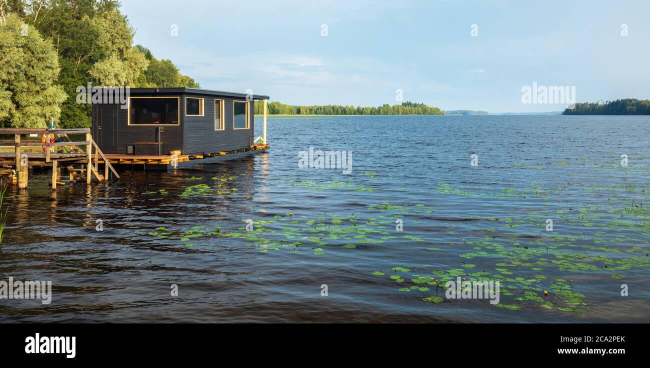 Galleggiante marrone casa galleggiante in legno con sauna ormeggiata per jetty al lago Suontee a Estate, Finlandia Foto Stock