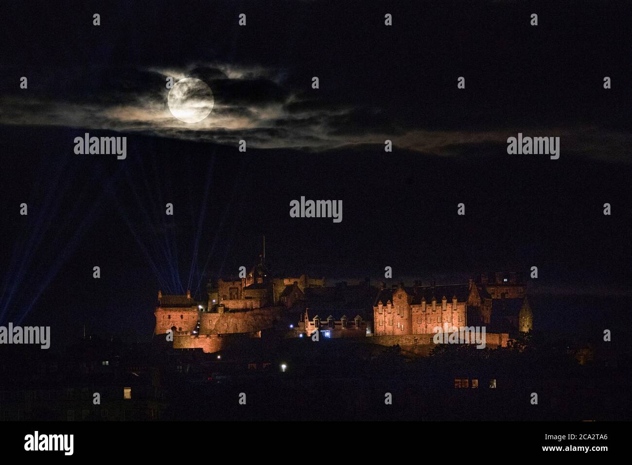 La luna piena, conosciuta come Sturgeon Moon nel mese di agosto, sorge attraverso le nuvole sopra il Castello di Edimburgo. Foto Stock
