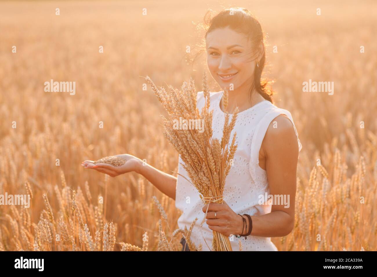 Donna che tiene covone di spighe di grano a campo agricolo Foto Stock