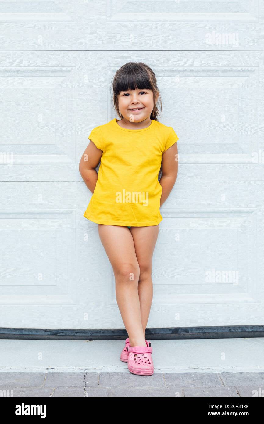 Adorabile bambina con capelli neri che indossa una camicia gialla appoggiata su sfondo bianco. Foto Stock