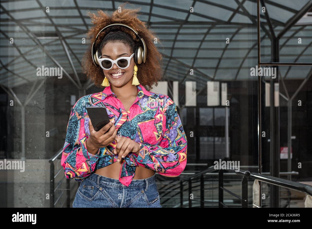 Contenuto African American femmina in abiti alla moda e occhiali da sole  navigare in internet sul telefono cellulare mentre si ascolta la musica in  cuffie wireless Foto stock - Alamy