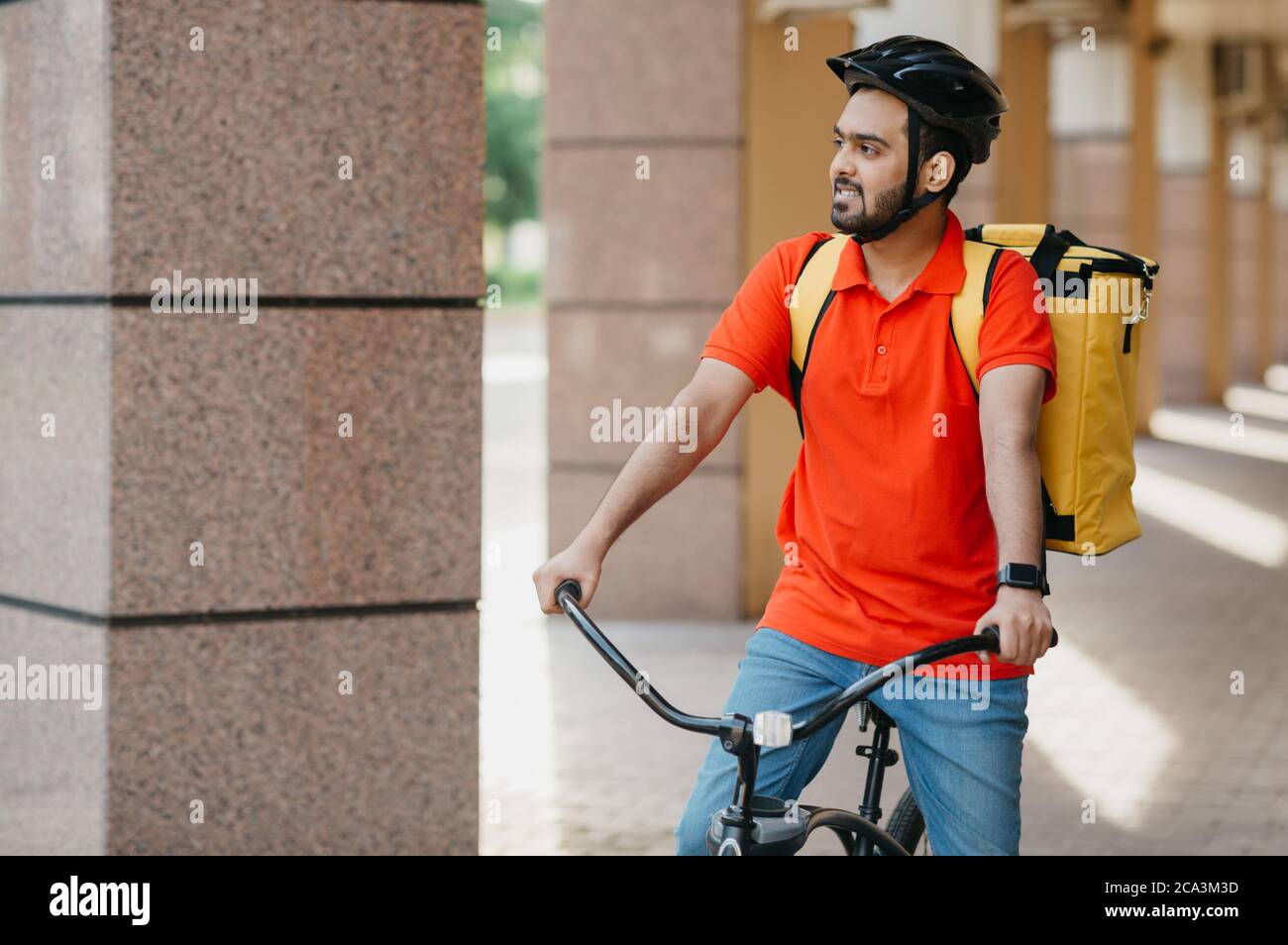 Lavoro attivo all'aperto. Ragazzo sorridente in casco con borsa gialla sulla bicicletta che guarda da parte Foto Stock