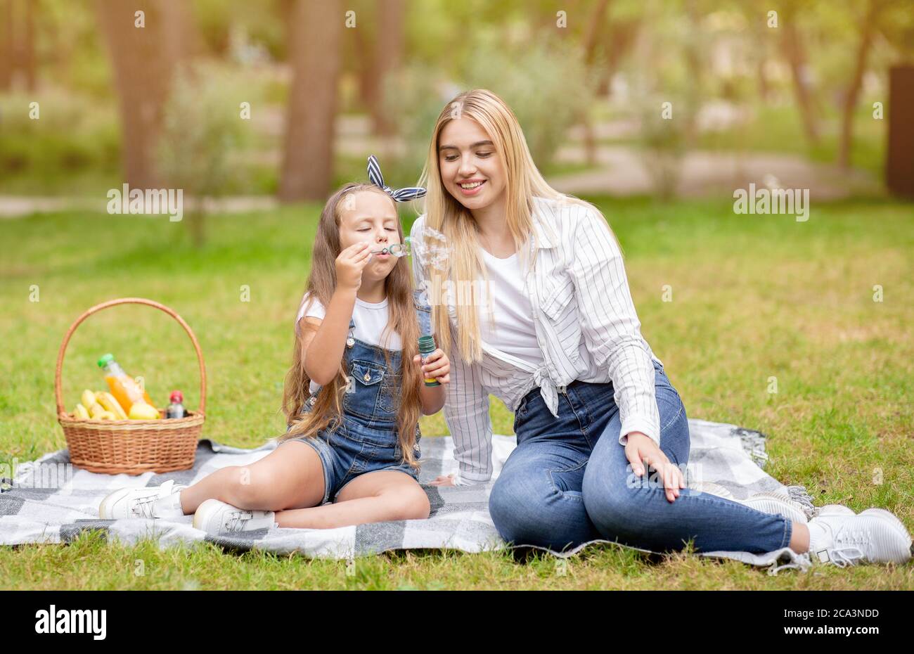 Sorridente madre e figlia che soffiano bolle di sapone rilassandosi a Park Foto Stock