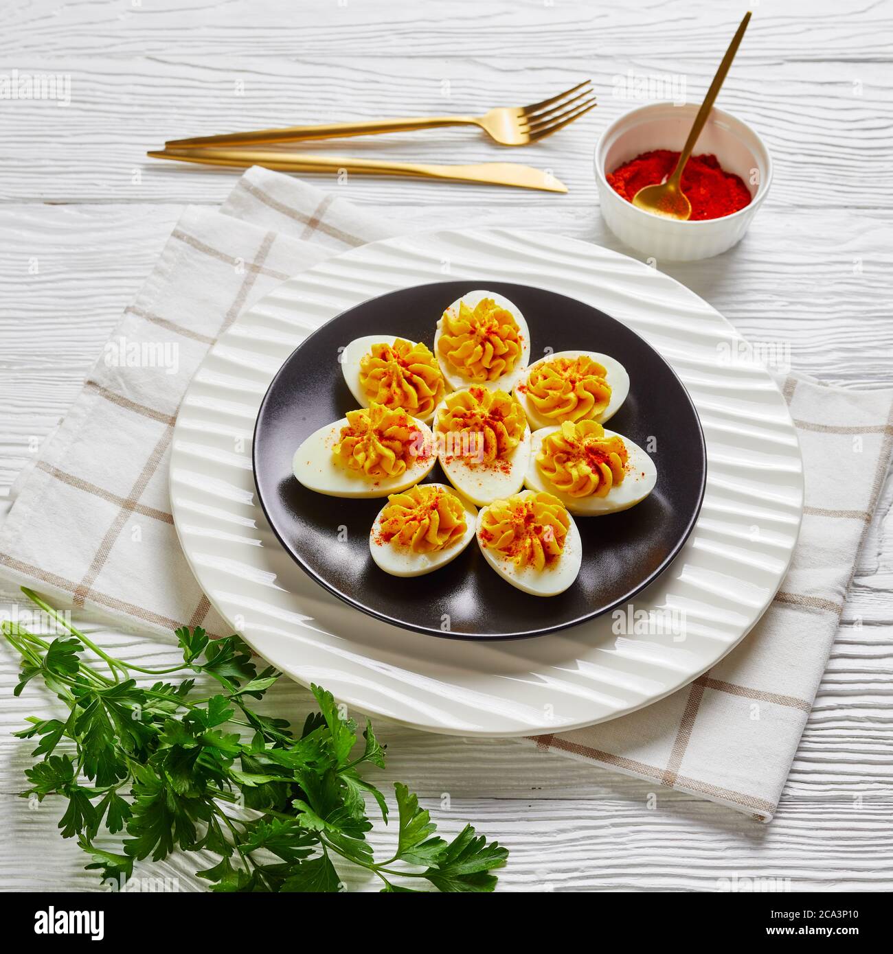 Uova devolate farcite con un mix di tuorli d'uovo, salsa di sriracha, maionese, aceto di sidro di mele cosparso di paprika affumicata su un piatto su un woo bianco Foto Stock