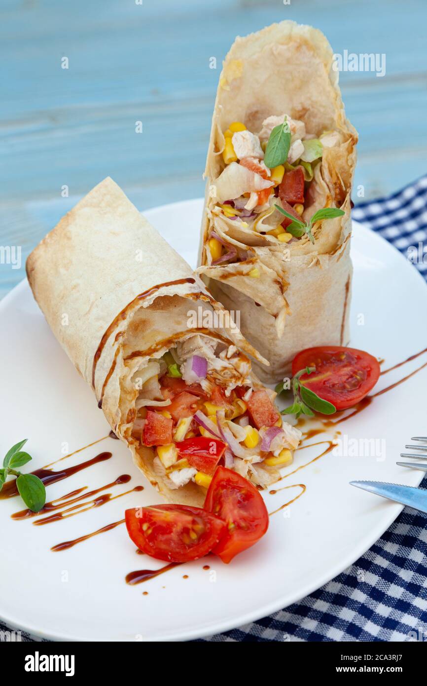 Burrito su un piatto bianco in un ristorante. Un pasto veloce di pollo fritto, salsa, cipolle rosse, mais, pomodori. Burritos avvolge con manzo e verdure. R Foto Stock