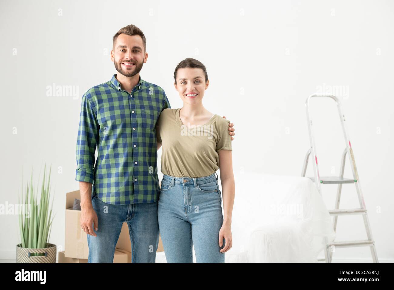 Ritratto di felice bella giovane coppia abbracciandosi in un nuovo appartamento vuoto con roba in movimento Foto Stock
