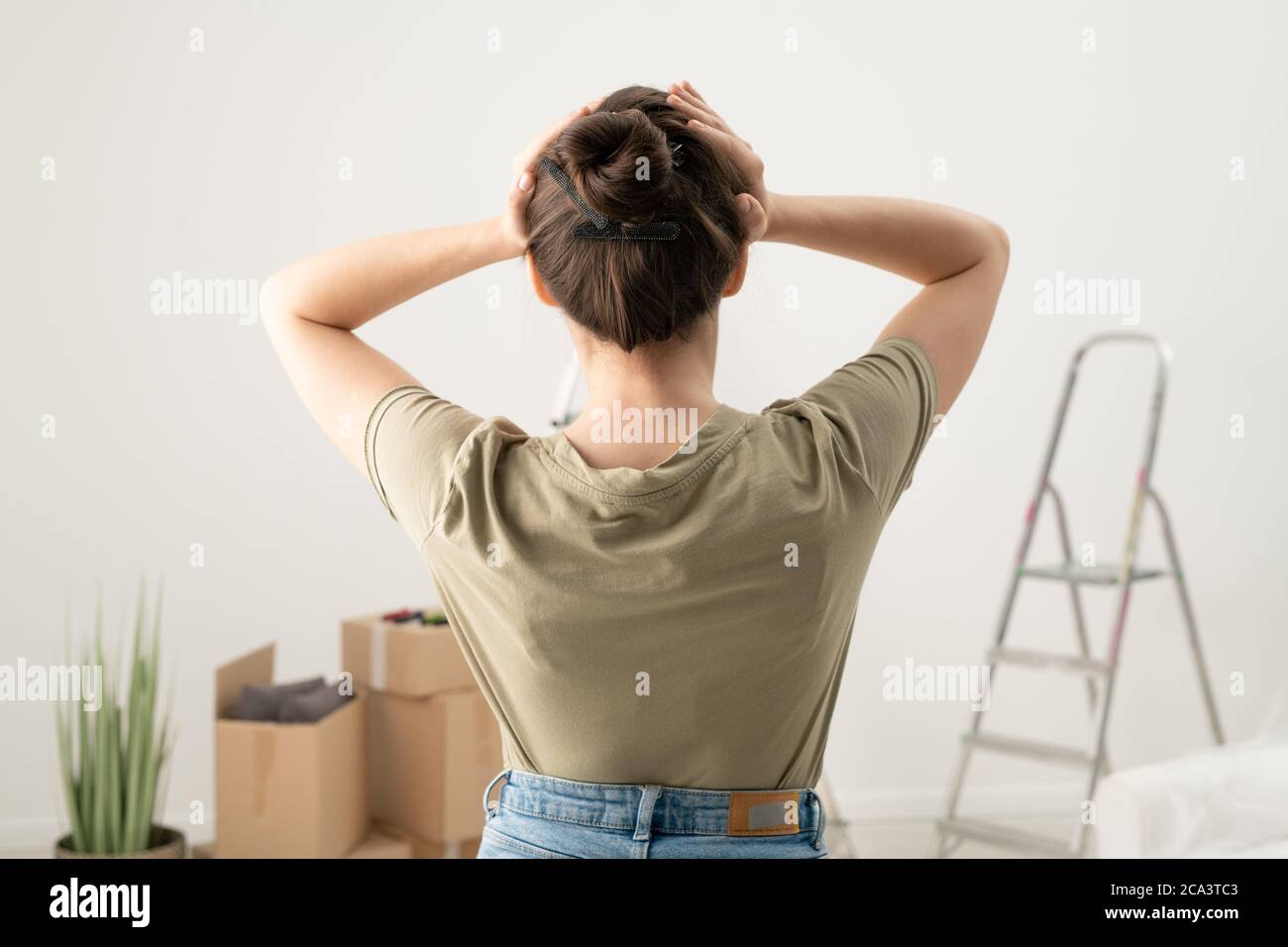 Vista posteriore della donna bruna che tiene la testa nelle mani mentre si sente mal di testa dal fissare le cose in appartamento Foto Stock