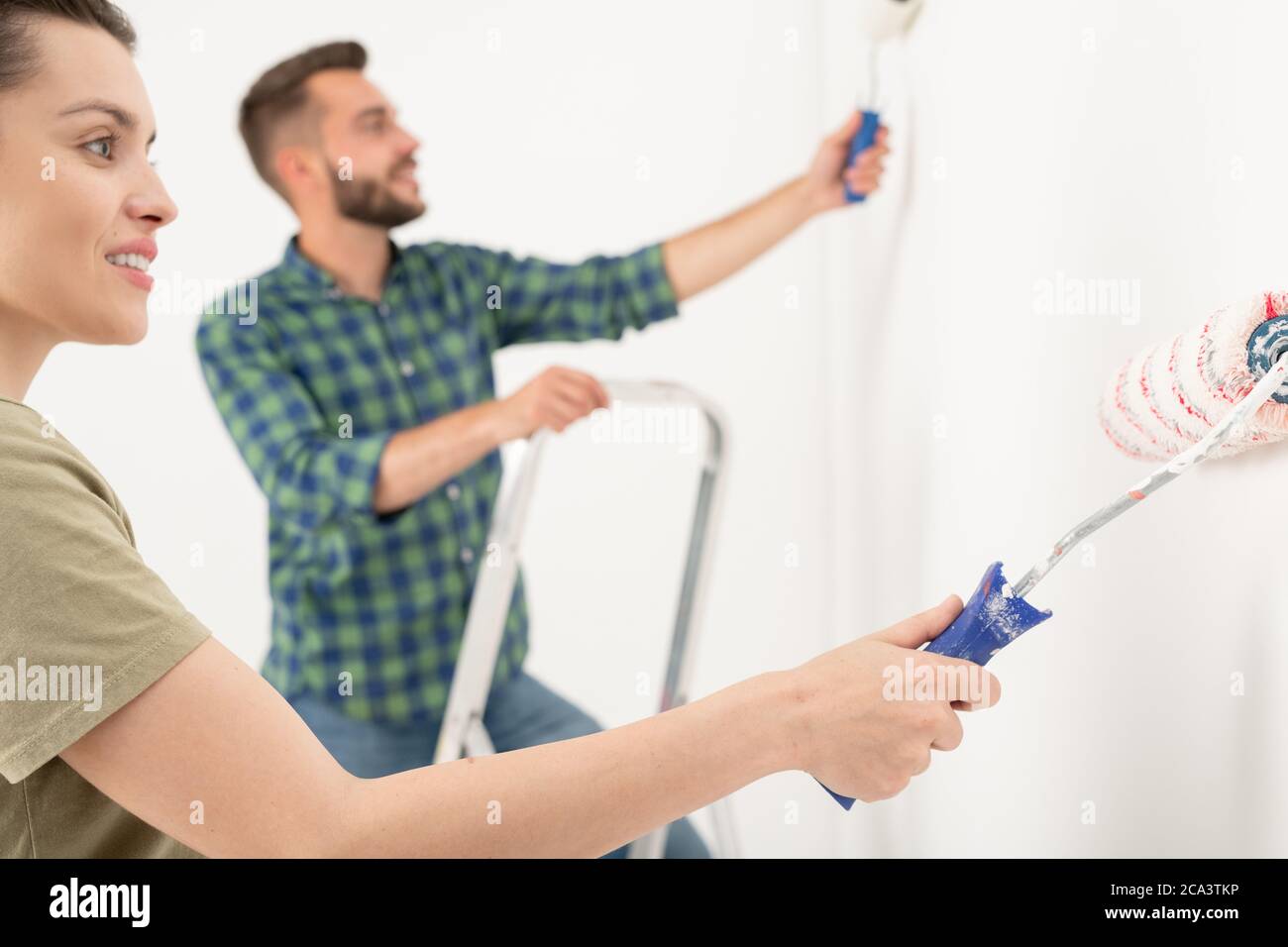 Sorridente giovane donna che spazza il rullo di vernice sulla parete mentre dipingono la stanza con il ragazzo Foto Stock